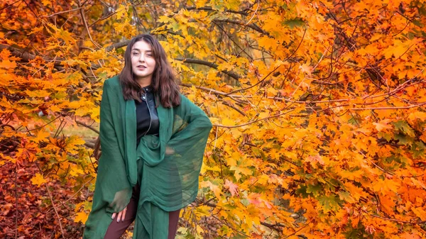 Güz parkında eşarplı genç bir kadın kameraya poz veriyor.