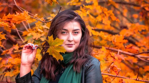 Güz parkında eşarplı genç bir kadın kameraya poz veriyor.