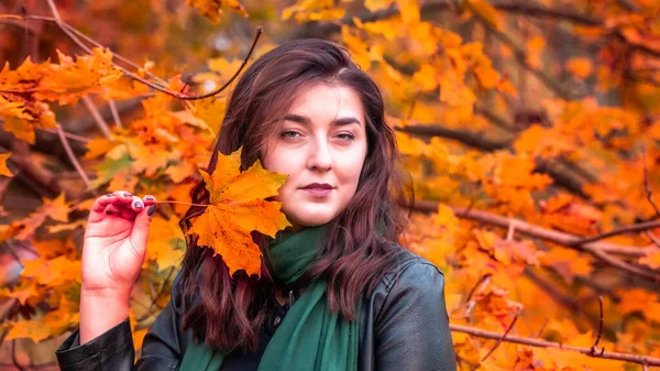 Güz parkında eşarplı genç bir kadın kameraya poz veriyor.