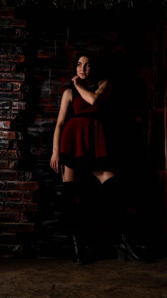 Muito jovem modelo sexy fêmea com cabelo escuro em vestido vermelho longo incrível e sapatos pretos posando no estúdio escuro — Fotografia de Stock