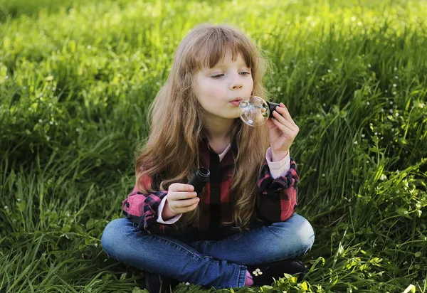 Liten flicka blåser såpbubblor i parken — Stockfoto