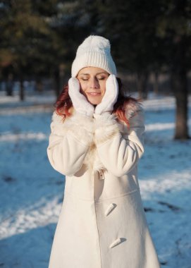 Şapkalı kızıl saçlı kadın dışarıda karla eğleniyor. Kadın kış mevsiminde ormanda yürüyor.