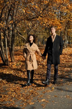 Mutlu genç çift sonbahar parkında eğleniyor. Genç bir kadın ve bir adam dışarıda yürüyor..