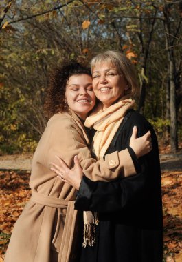 Anneye kız bakımı. Orta yaşlı kadın ve genç kıvırcık saçlı kadın sonbahar parkında kocaman..