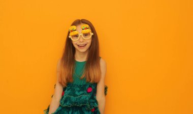 Yeşil şenlik elbisesi ve noel gözlüğü takmış şirin bir çocuk. Sarı arka planda fotokopi çekiliyor..