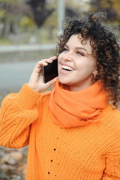 Smiling Curly Hair Beautiful Young Woman Orange Sweater Speaking Mobile — Stock Photo, Image