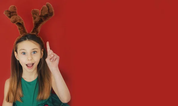 穿着绿色节日服装 穿着红色背景和复制空间的鹿耳 微笑着情绪化的女孩 圣诞节的概念 — 图库照片