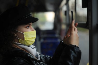 Otobüste koruyucu maskeli genç bir kadın, karantina önlemlerini gözlemliyor ve QR kodunu tarıyor.