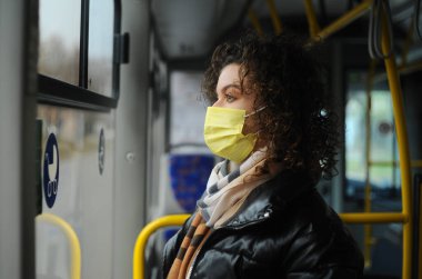 Koruyucu maskeli üzgün genç bir kadın otobüse biniyor ve karantina önlemlerini izliyor..