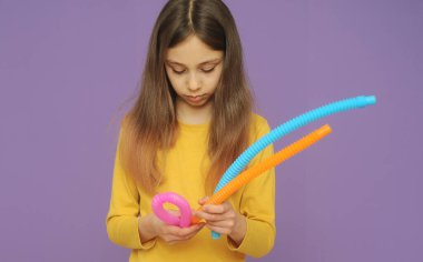 Sarı elbiseli küçük akıllı kız popüler oyuncak pop tüpleriyle oynuyor.