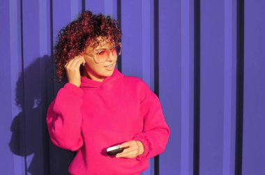 Mor kapüşonlu, kıvırcık pembe saçlı kadın menekşe arka planda poz veriyor.. 