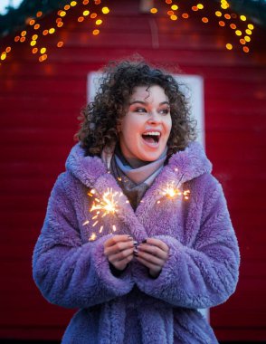 Smiling woman in trendy violet coat with sparkles on red festive background