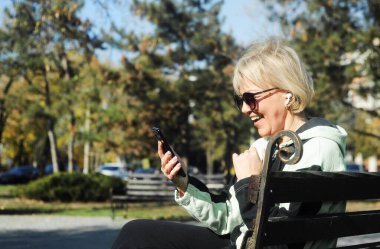 Middle aged woman holding mobile phone in hands outdoors. Beautiful mature woman 50s with mobile phone messaging outside 