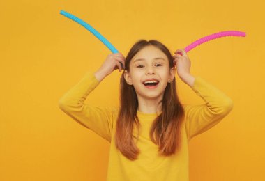 Smart girl in yellow clothes plays with trendy toy pop tube.