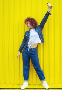 Smiling young woman in pinnk sunglasses on yellow background outdoors