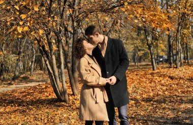 Koyu renk ceketli genç bir adam ve açık havada kahve içen bej paltolu bir kadın. Güz parkında düşen yapraklarla kahve içen genç ve güzel bir çift.. 