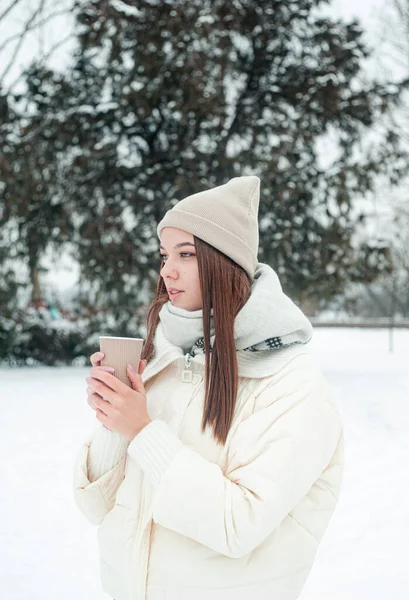 屋外でお茶を飲む女性の肖像画 雪の日の公園では 熱い飲み物のカップを持つ若い女性が楽しいです — ストック写真