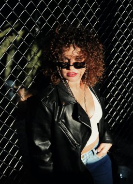 Güneş gözlüklü, deri ceketli, esmer, şık kıvırcık saçlı kadın.. 
