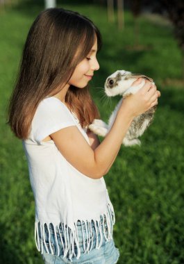 Kız dışarıda bebek tavşana sarılıyor.
