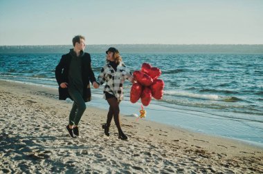 Kumsalda kırmızı kalp balonları olan mutlu koşu çifti