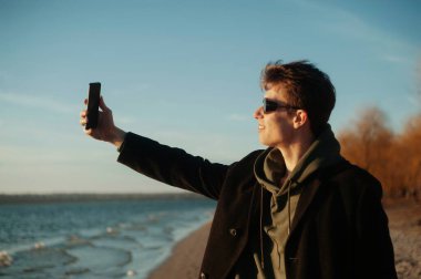 Genç adam sahilde selfie çekiyor.