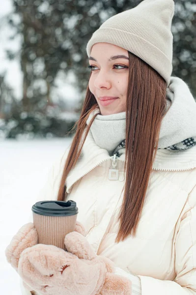 밖에서 마시는 뜨거운 음료를 마시는 여자는 눈내리는 날씨에 공원에서 재미를 — 스톡 사진