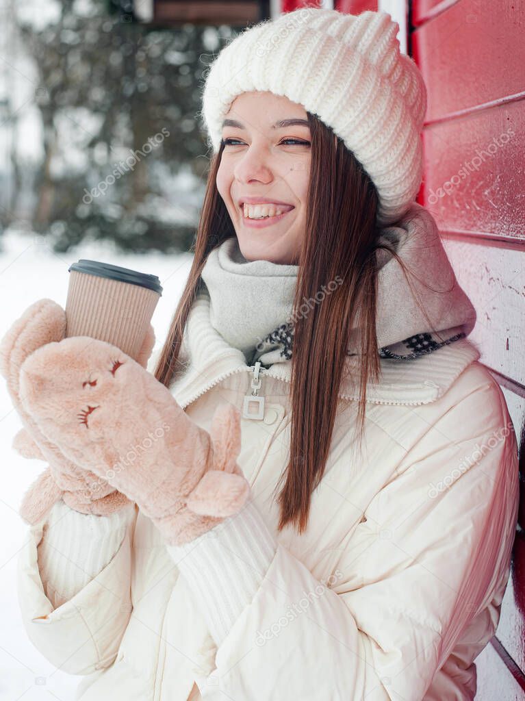  Portrait of woman drinking tea outdoors. Young woman with a cup of hot drink has fun in park in snowy weather.