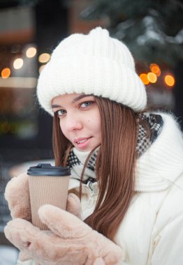 Smiling young woman drinking coffee in snowy forest. Winter vacation.
