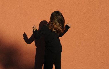 Tatlı küçük kız turuncu arka planda gölge tiyatrosunda oynuyor..