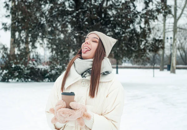 屋外でお茶を飲む女性の肖像画 雪の日の公園では 熱い飲み物のカップを持つ若い女性が楽しいです — ストック写真
