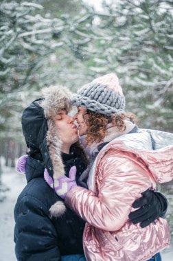 Young beautiful couple in winter forest. Happy couple has fun with snow.