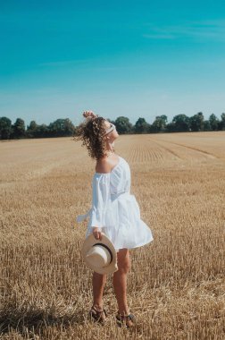 portrait of young curly haired woman in white dress with a white sunglasses posing in the wheat field