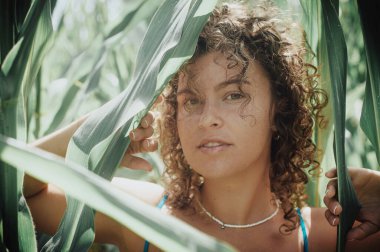 beautiful curly haired woman with green leaves in a corn field on a sunny day