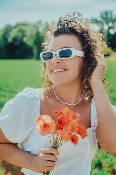 young woman with curly hair in a white dress with a bouquet of poppies flowers