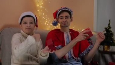 Noel Tatili 'nde iki mutlu adam kanepede oturup ellerinde hediyelerle dans ediyorlar. Noel Baba şapkasıyla. Noel zamanı. Mutluluk