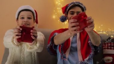 Noel tatilinde iki adam kameraya hediye gösterir. Duygular. Noel Baba şapkasıyla. Hediye. Noel.