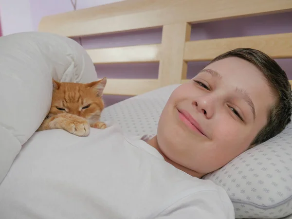 Jongen en kat liggen in bed. Emoties van geluk en vreugde. Live stijl. kopieerruimte — Stockfoto
