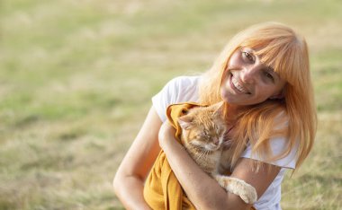 Güzel gözleri olan güzel bir kedi. Kızıl kedi. Kızıl saçlı bir kız kırmızı bir kedi tutuyor. Kız ve kedi. Pankart. Boşluğu kopyala