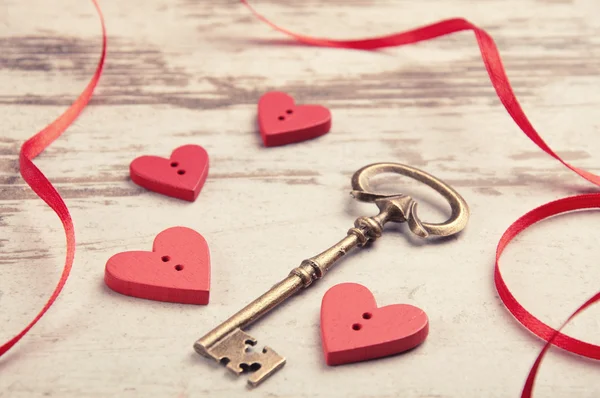 Red wooden hearts on wooden board with key and ribbon — Stock Photo, Image