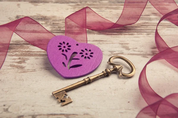 Violet wooden heart on wooden desk with key and ribbon — Stock Photo, Image