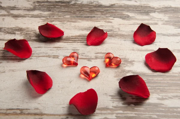 Corazones rojos en el tablero de madera con pétalos — Foto de Stock