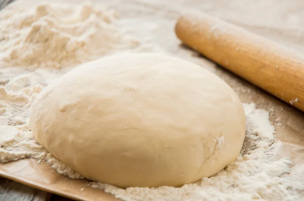 wooden rolling pin with freshly prepared dough for pizza