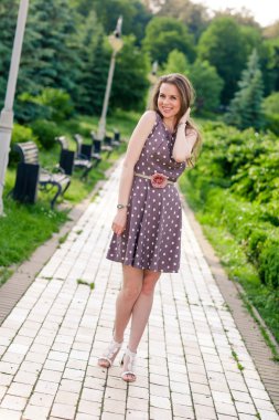 Güzel genç bir kadın yaz parkında yolda yürüyor.