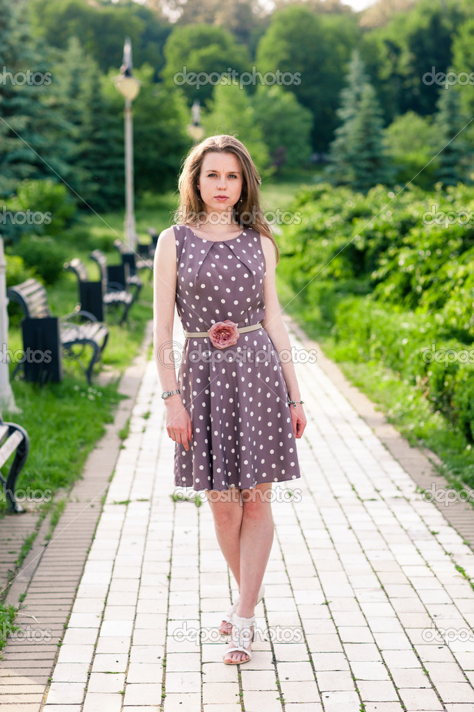 Beautiful young woman walking along the road in summer park