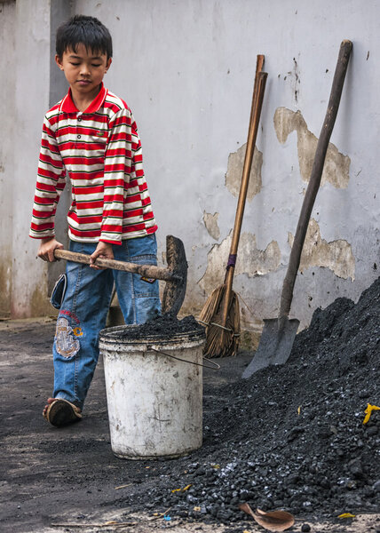 Boy scoops coal in bucket to take inside home.