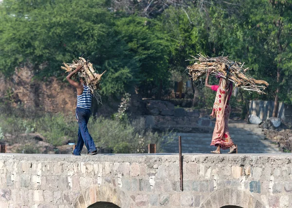 Indien Orchha - Februar 2011 - Paar, Mann und Frau in Sari, tragen Brennholz auf dem Kopf über Brücke. — Stockfoto