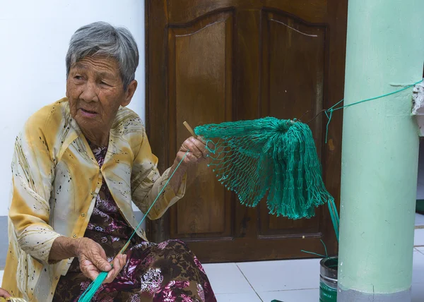 老婦人は彼女の家の前で漁網を編む. — ストック写真