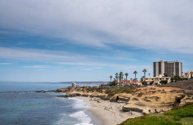 La Jolla, California, ABD - 3 Ekim 2021: Kahverengi kaya oluşumu ve Wipeout Beach 'teki mağaraların mavi bulutların altında yüksek apartman binaları.