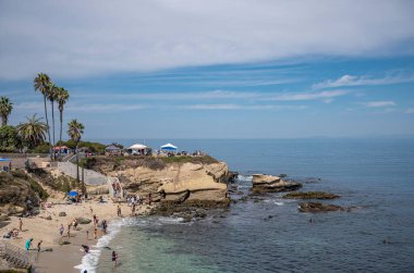 La Jolla, California, ABD - 3 Ekim 2021: Blue Cloudscape 'in altında, Cove sahilinin üstündeki kayalık kayalıklarda Point La Jolly' ye bakın. Giysi renk katar. 