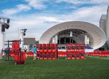 San Diego, California, ABD - 4 Ekim 2021: Jacobs Park 'taki White Rady Shell konser salonu. İşçiler mavi bulutların altında yeşil çimlere kırmızı sandalyeler kurdular.